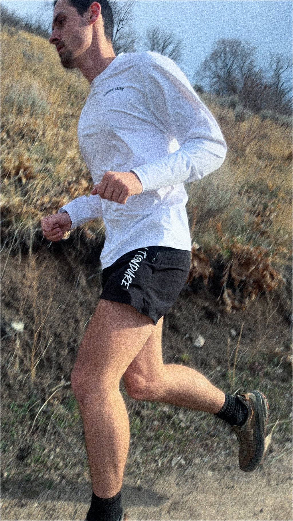 Man running on a trail wearing a white long-sleeve shirt and black shorts.