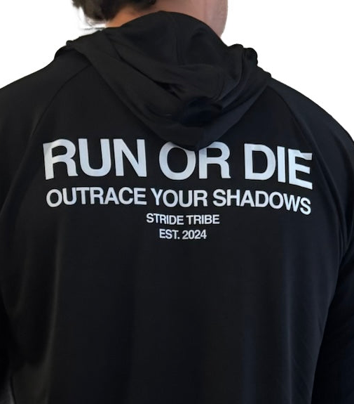 A close-up back view of a person wearing a black hooded athletic top with large white text reading 'RUN OR DIE' and 'OUTRACE YOUR SHADOWS,' plus smaller 'STRIDE TRIBE EST. 2024' text.